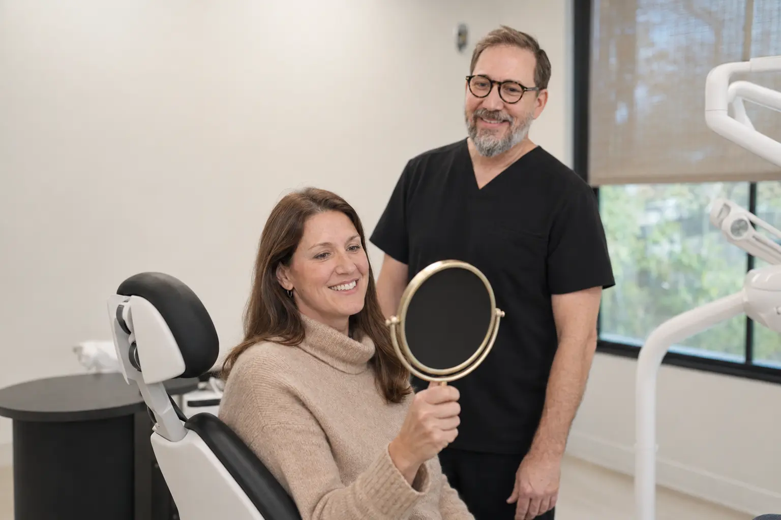 Patient in the dental chair checking her smile in a hand mirror